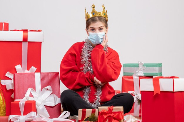 Vue de face jeune femme assise avec des cadeaux de Noël en masque et couronne