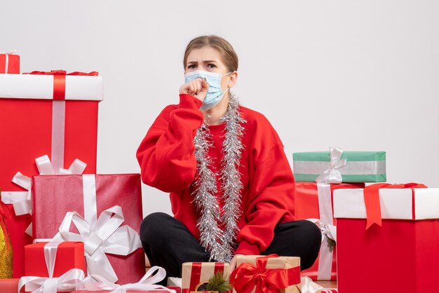 Vue de face jeune femme assise avec des cadeaux de Noël en masque stérile