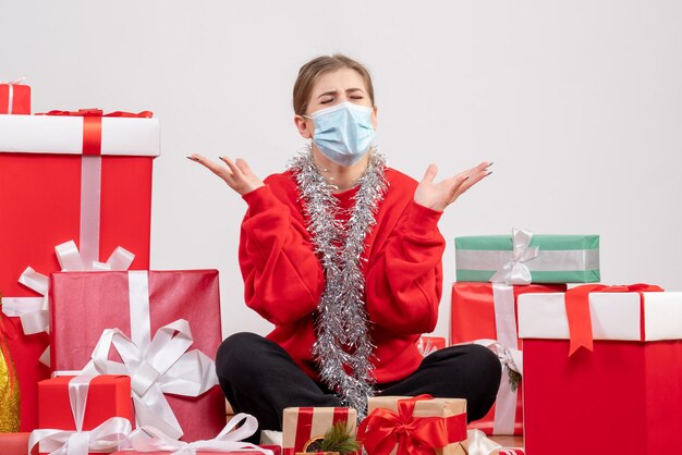 Vue de face jeune femme assise avec des cadeaux de Noël en masque stérile