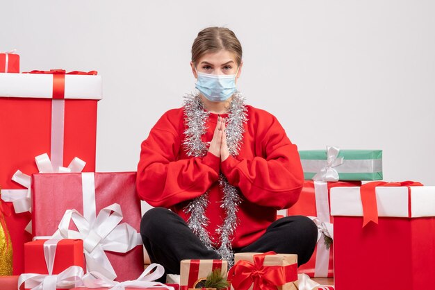 Vue de face jeune femme assise avec des cadeaux de Noël en masque stérile