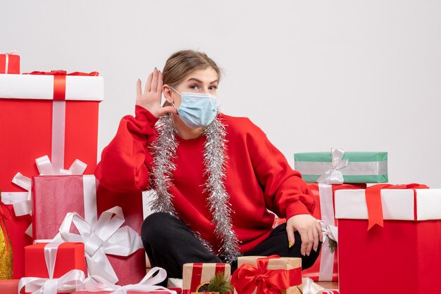 Vue de face jeune femme assise avec des cadeaux de Noël en masque stérile