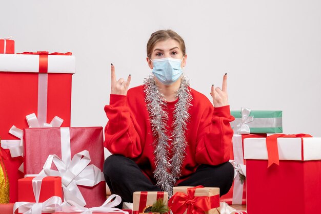 Vue de face jeune femme assise avec des cadeaux de Noël en masque stérile