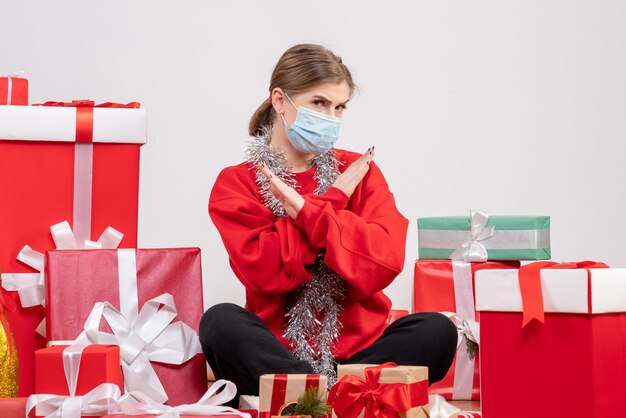 Vue de face jeune femme assise avec des cadeaux de Noël en masque stérile