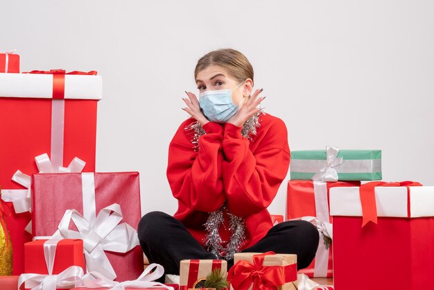 Vue de face jeune femme assise avec des cadeaux de Noël en masque stérile