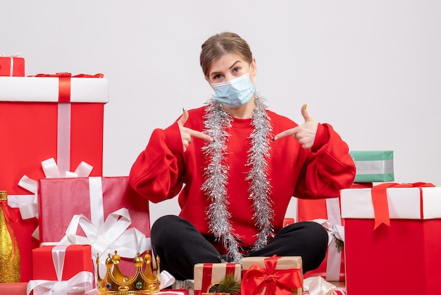 Vue de face jeune femme assise avec des cadeaux de Noël en masque stérile