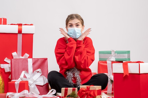 Vue de face jeune femme assise avec des cadeaux de Noël en masque stérile