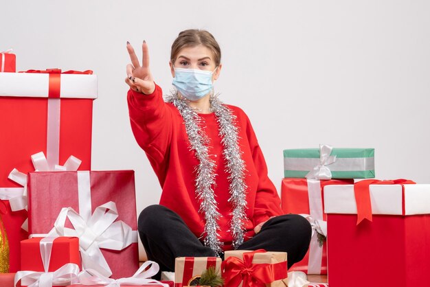 Vue de face jeune femme assise avec des cadeaux de Noël en masque