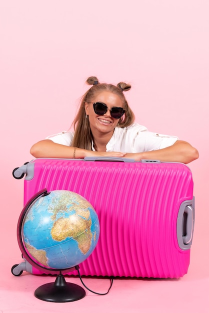 Vue de face d'une jeune femme assise avec son sac rose et se préparant pour des vacances sur le mur rose