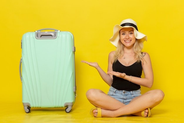 Vue de face jeune femme assise avec son sac vert se sentir heureux sur mur jaune voyage vacances soleil voyage voyage