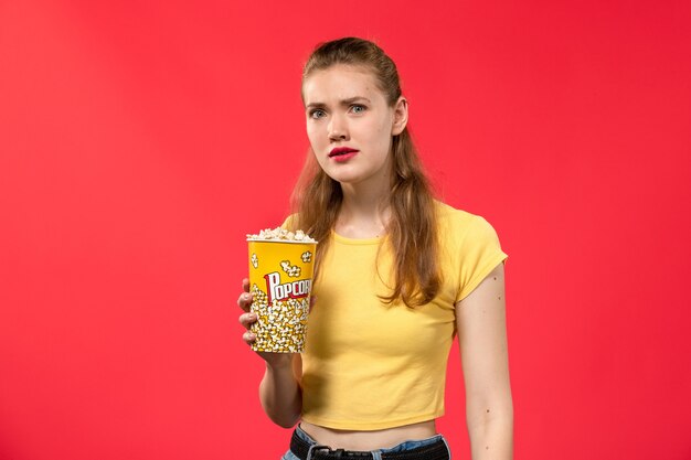 Vue de face jeune femme au cinéma holding pop-corn avec expression confuse sur mur rouge cinéma cinéma snack femme film amusant