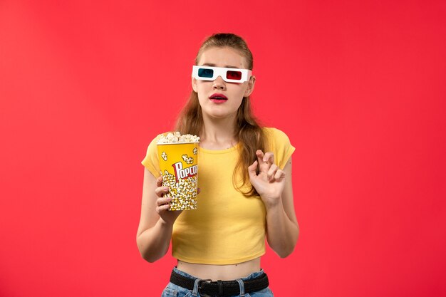 Vue de face jeune femme au cinéma holding pop-corn en d lunettes de soleil sur le mur rouge cinéma cinéma femme fun film