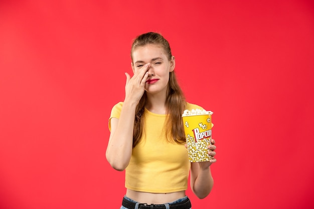 Vue de face jeune femme au cinéma holding pop-corn sur le mur rouge cinéma cinéma cinéma couleurs féminines