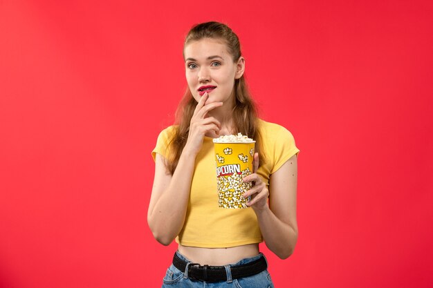 Vue de face jeune femme au cinéma holding pop-corn sur le mur rouge cinéma cinéma cinéma femme fun time film