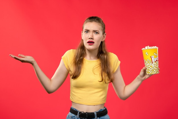 Vue de face jeune femme au cinéma holding pop-corn sur le mur rouge cinéma salle de cinéma snack cinéma femme fun film