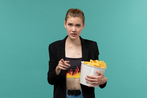 Vue de face jeune femme au cinéma manger des chips de pomme de terre regarder un film sur une surface bleue