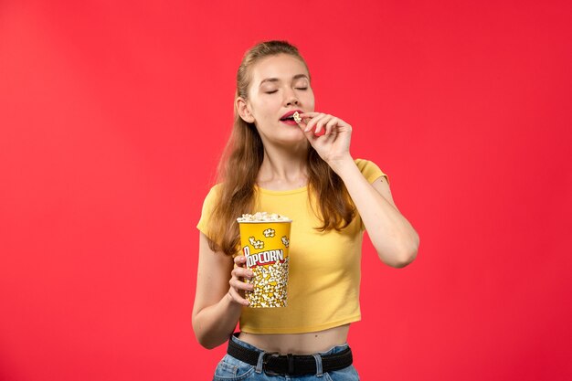 Vue de face jeune femme au cinéma tenant du pop-corn et manger sur le mur rouge films théâtre cinéma film fille