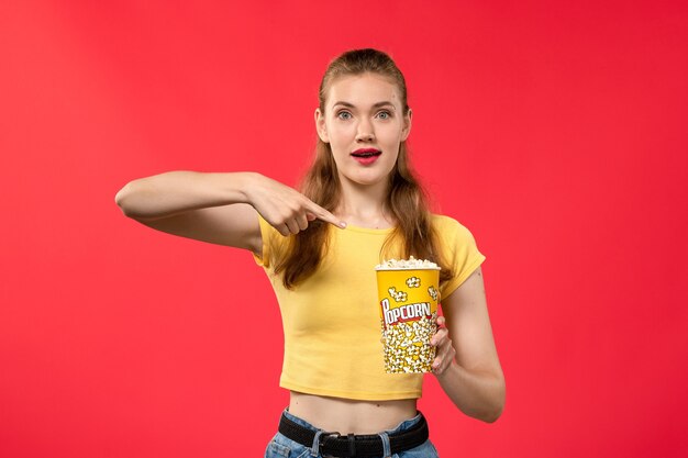 Vue de face jeune femme au cinéma tenant du pop-corn et posant sur le mur rouge films théâtre cinéma snack femme film amusant