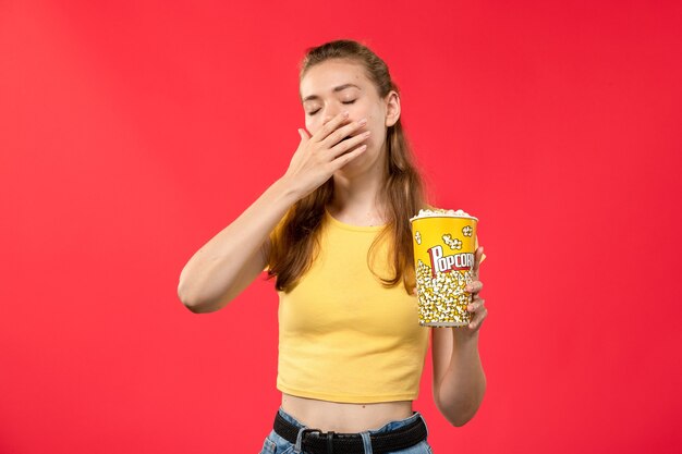 Vue de face jeune femme au cinéma tenant le paquet de pop-corn et bâillant sur le mur rouge films cinéma cinéma fun film féminin