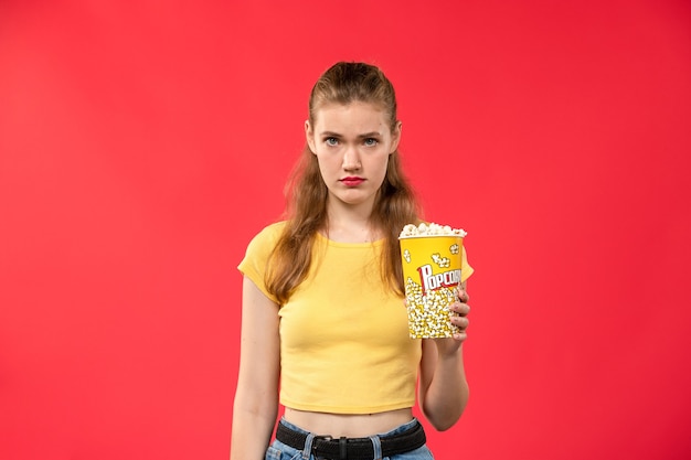 Vue de face jeune femme au cinéma tenant le paquet de pop-corn avec expression déprimée sur le mur rouge films cinéma cinéma film