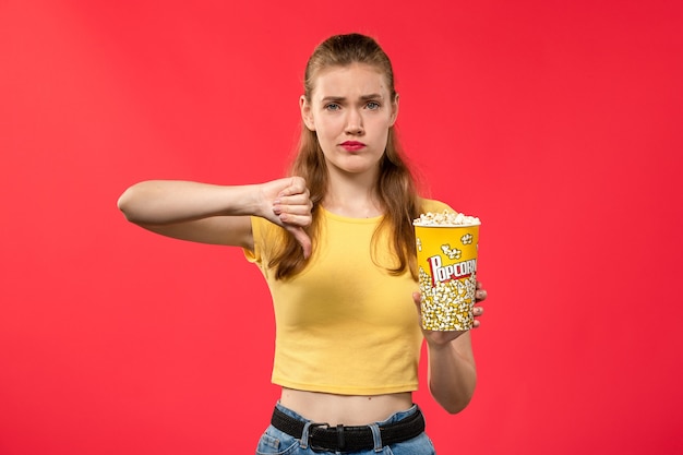 Vue de face jeune femme au cinéma tenant le paquet de pop-corn et montrant contrairement au signe sur le mur rouge films théâtre cinéma snack fun film