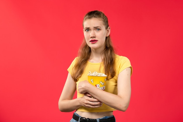 Vue de face jeune femme au cinéma tenant le paquet de pop-corn sur mur rouge clair films cinéma cinéma fun film