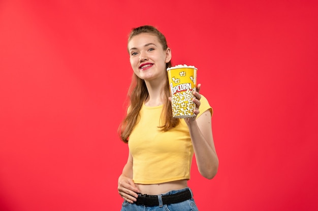 Vue de face jeune femme au cinéma tenant le paquet de pop-corn avec sourire en -d lunettes de soleil sur mur rouge films cinéma cinéma fun film
