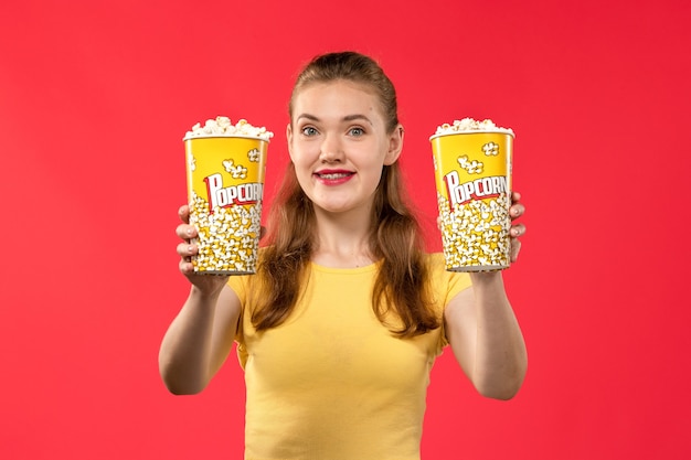 Vue de face jeune femme au cinéma tenant des paquets de pop-corn sur le mur rouge clair cinéma cinéma femme fun film