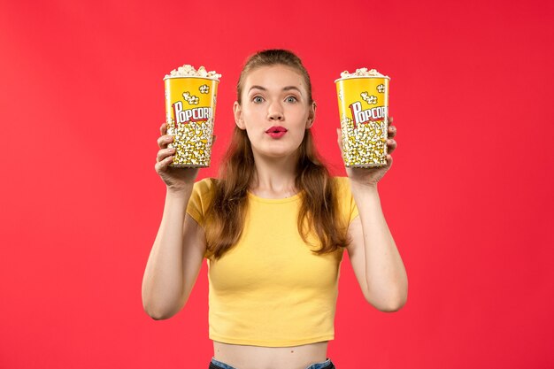 Vue de face jeune femme au cinéma tenant des paquets de pop-corn sur le mur rouge films théâtre cinéma snack femme film amusant