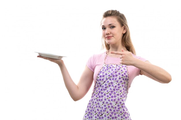 Une vue de face jeune femme au foyer attrayante en chemise rose cape colorée tenant une assiette blanche souriant posant sur le fond blanc cuisine cuisine femme