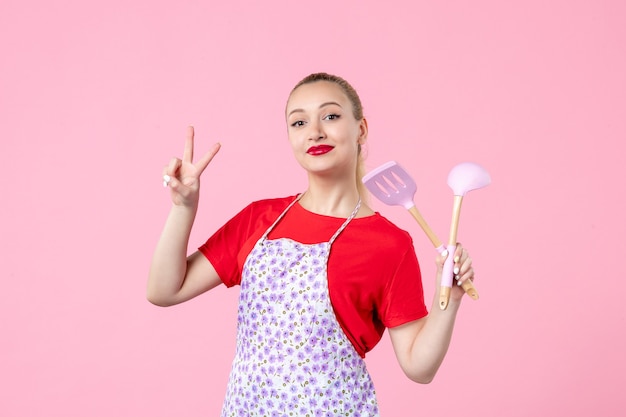 Vue de face jeune femme au foyer avec des couverts dans ses mains sur un mur rose