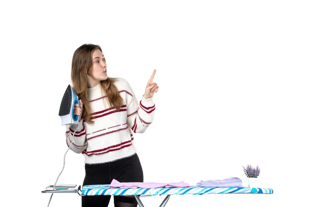 Vue de face jeune femme au foyer avec planche à repasser tenant un fer sur un fond blanc vêtements blanchisserie maison travaux ménagers femme travail de nettoyage