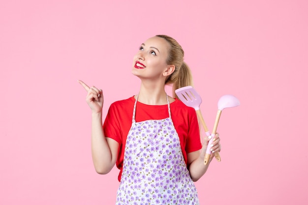 Vue de face jeune femme au foyer posant avec des couverts dans ses mains sur un mur rose