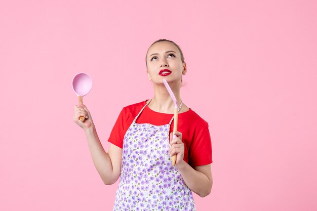 Vue de face jeune femme au foyer posant avec des couverts sur un mur rose