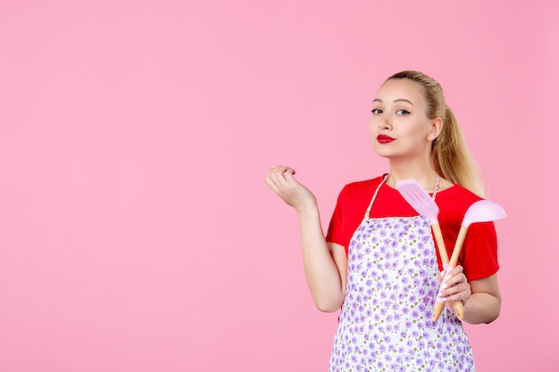 Vue de face jeune femme au foyer posant avec des couverts sur un mur rose