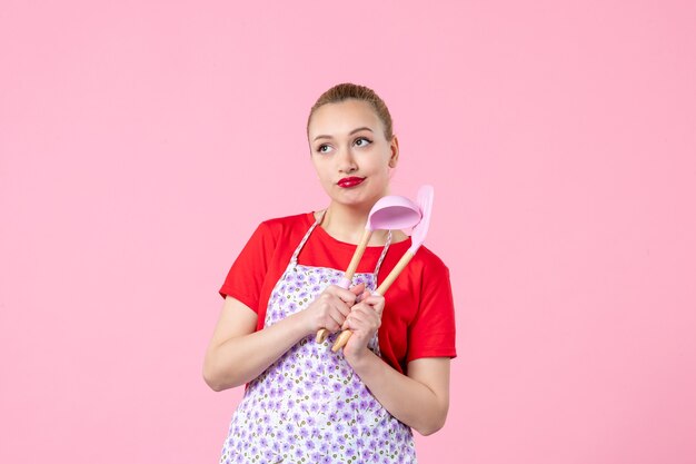 Vue de face jeune femme au foyer posant avec des couverts sur un mur rose