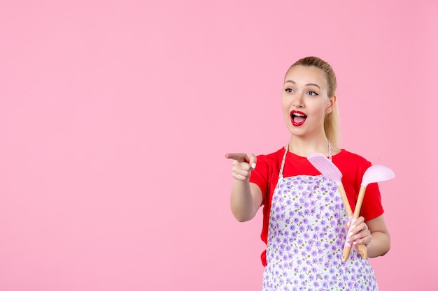 Vue de face jeune femme au foyer tenant des couverts et interagissant avec quelqu'un sur un mur rose