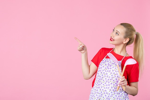 Photo gratuite vue de face jeune femme au foyer tenant des couverts sur un mur rose