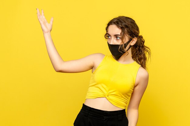 Vue de face de la jeune femme au masque noir sur le mur jaune