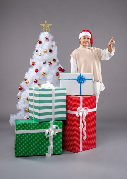 Vue de face jeune femme autour des cadeaux de vacances sur le bureau gris cadeau de nouvel an de Noël