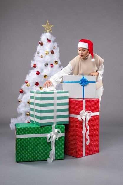 Vue de face jeune femme autour des cadeaux de vacances sur un bureau gris Noël féminin nouvel an