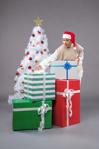 Vue de face jeune femme autour des cadeaux de vacances sur un bureau gris Noël féminin nouvel an