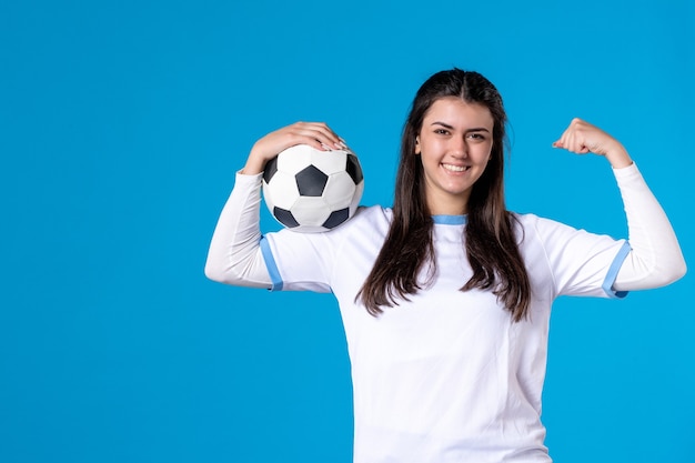 Vue de face jeune femme avec ballon de foot sur mur bleu