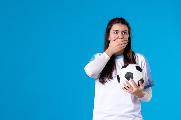 Vue de face jeune femme avec ballon de foot sur mur bleu