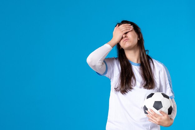 Vue de face jeune femme avec ballon de foot sur mur bleu