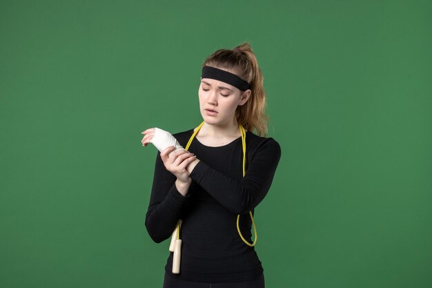 Vue de face jeune femme avec un bandage autour de son bras blessé sur fond vert athlète de sport douleur santé blessure femme entraînement couleur du corps