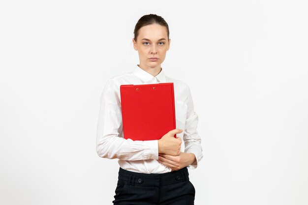 Vue de face jeune femme en blouse blanche avec dossier rouge dans ses mains sur fond blanc bureau émotions féminines modèle de sentiment