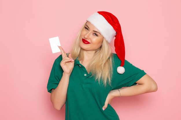 Vue de face d'une jeune femme en bonnet rouge tenant une carte blanche sur le mur rose