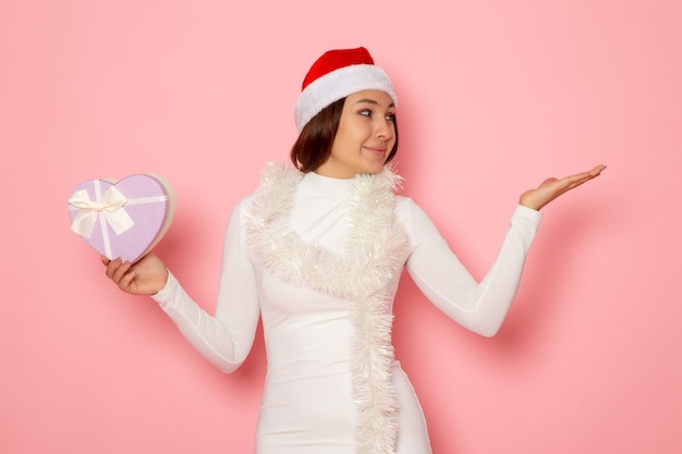 Vue de face d'une jeune femme en bonnet rouge tenant un présent en forme de coeur sur un mur rose