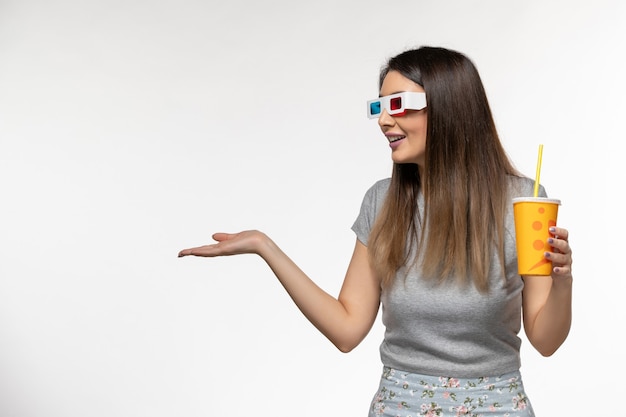 Vue de face jeune femme buvant du soda dans des lunettes de soleil sur la surface blanche légère