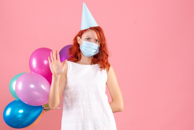 Vue de face jeune femme cachant des ballons colorés dans un masque stérile sur fond rose fête du nouvel an covid- couleur de Noël